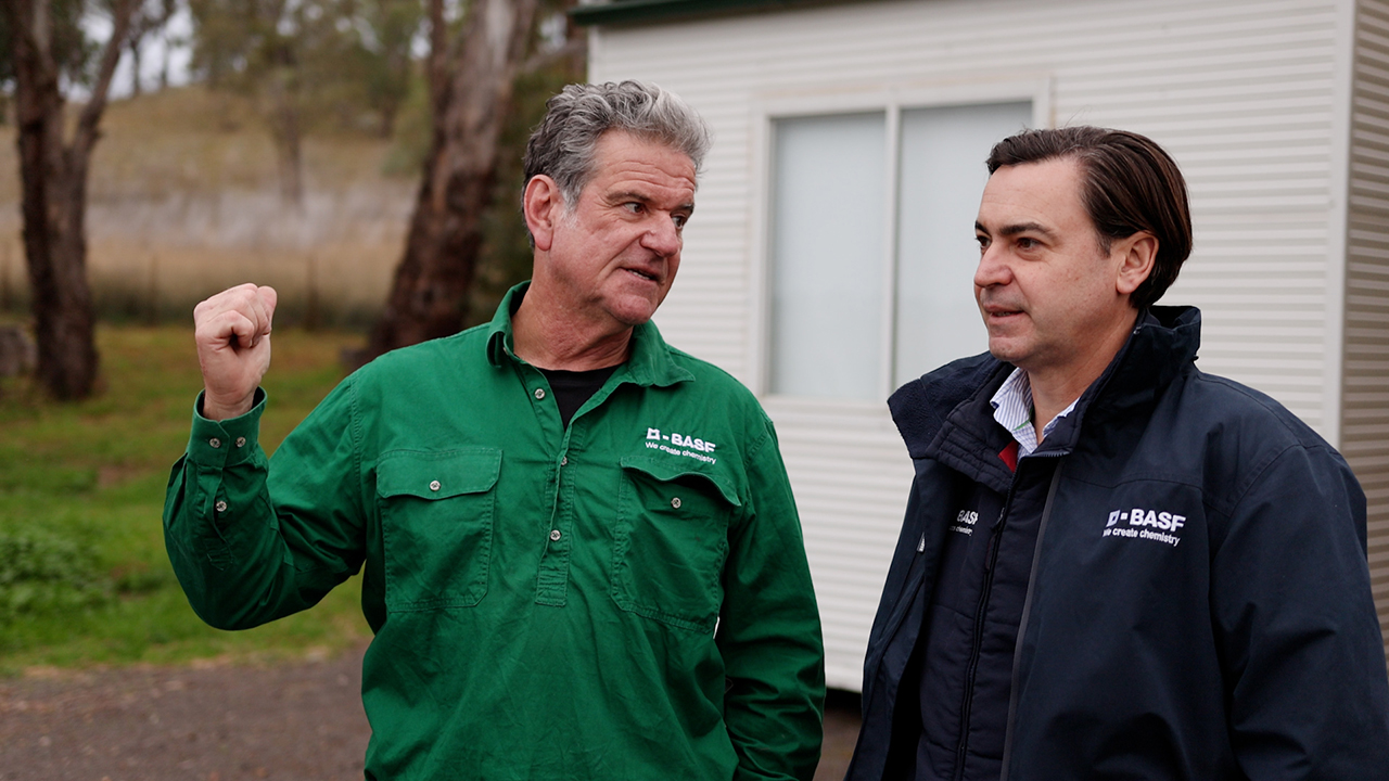 A man in a green button up shirt talking to a man in a navy jumper