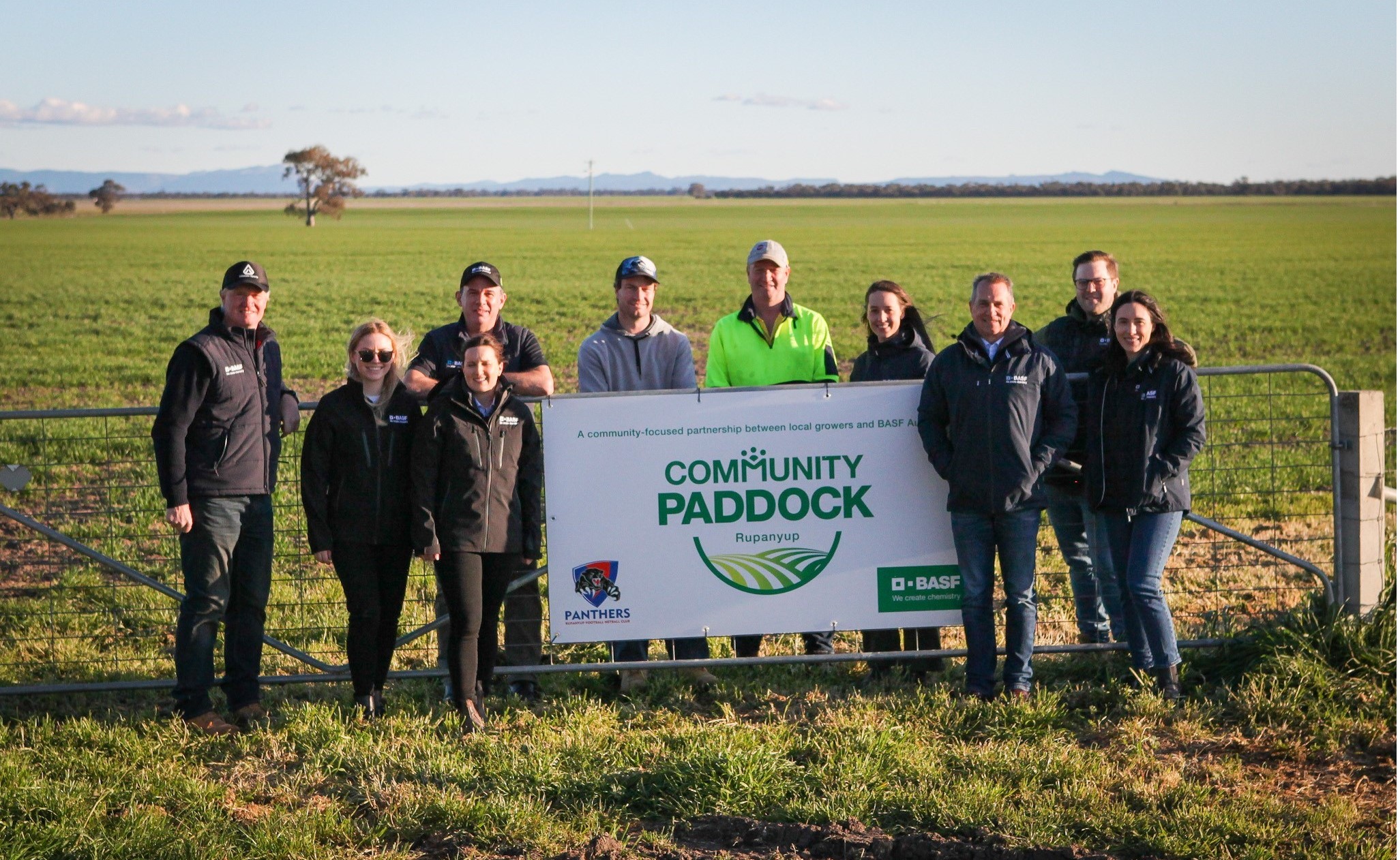 a group of people standing beside a sign that reads community paddock