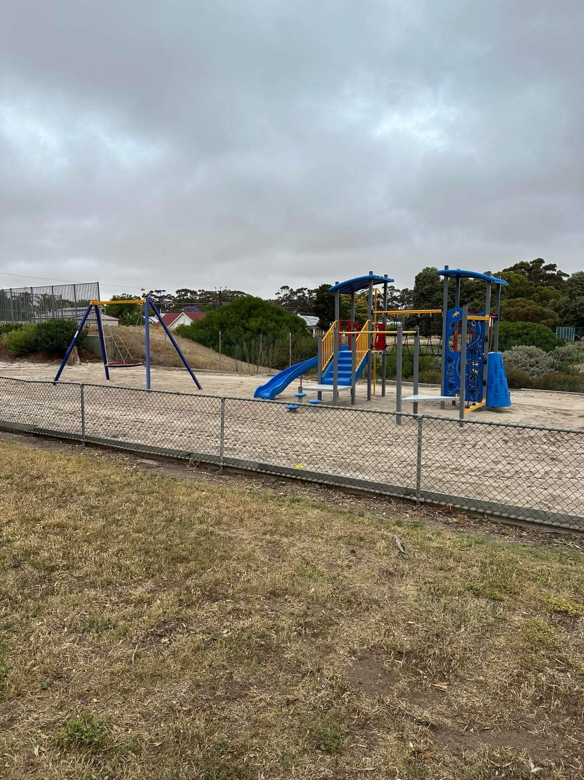 A playground with a big swing, a blue slide, blue steps and blue climbing apparatus