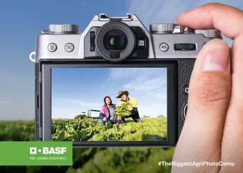 a hand holding a camera taking a photo of a man and woman in a crop field